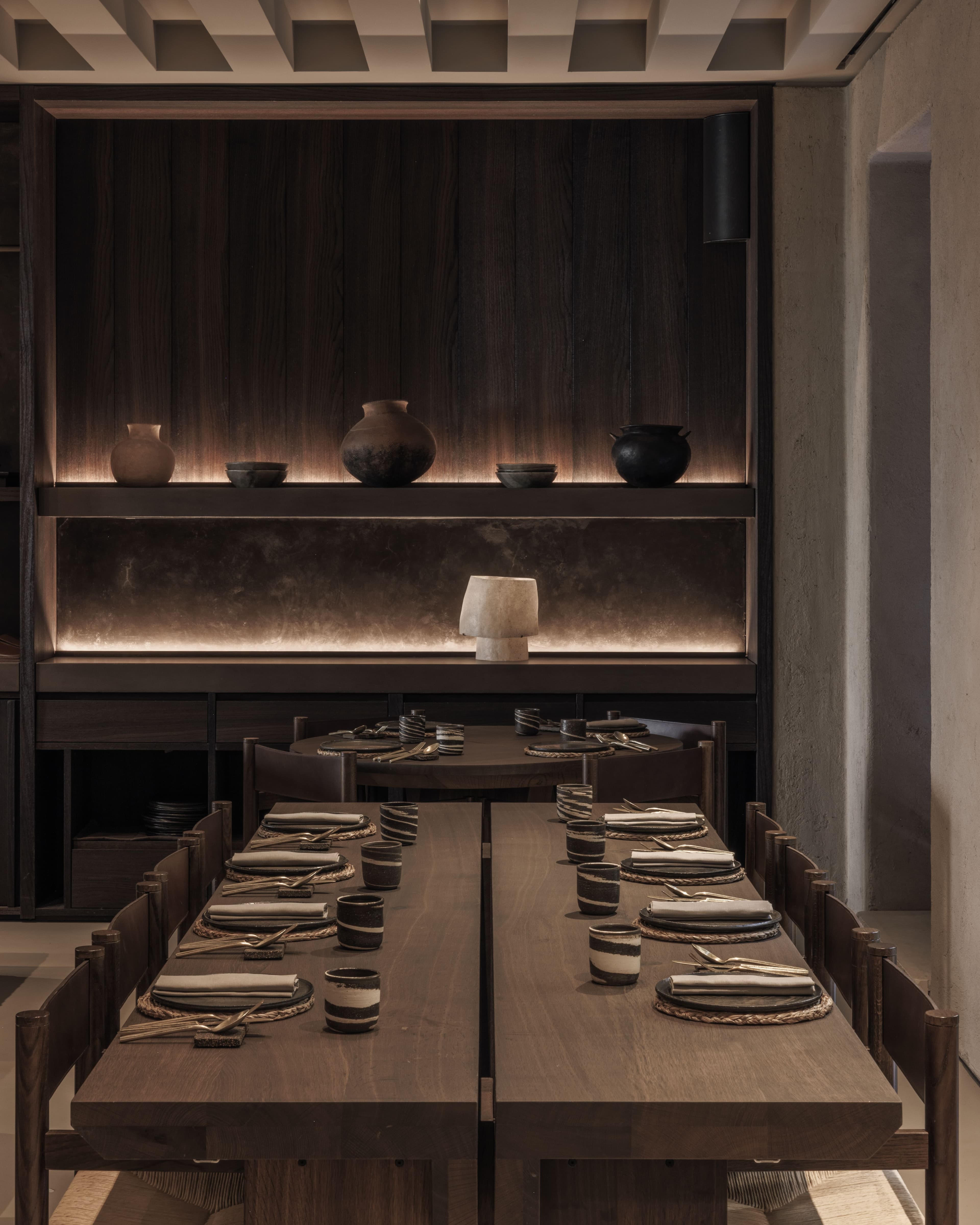 Sala privata YAPA con tavolo lungo apparecchiato, mensole retroilluminate con ceramiche artigianali