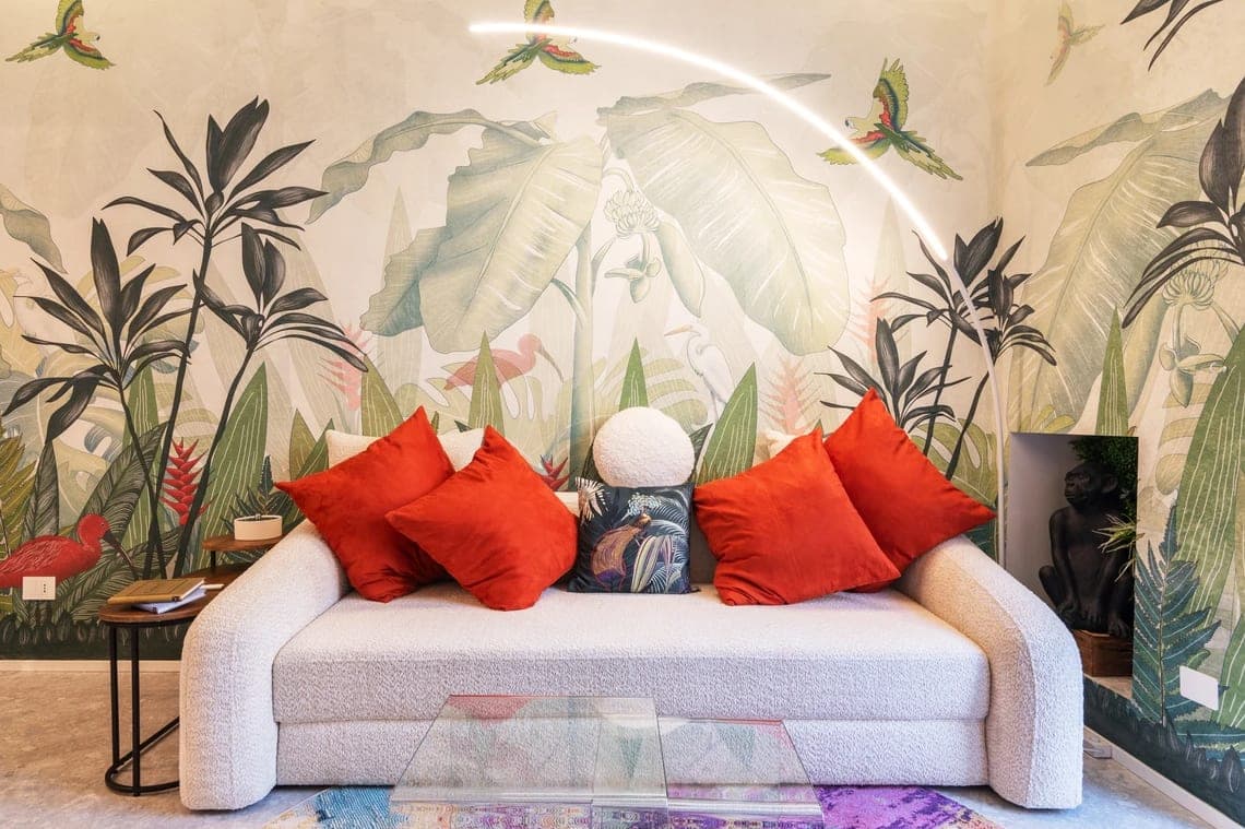 Divano bianco con cuscini botanici e luce LED ad arco davanti alla carta da parati tropicale con pappagalli e fenicotteri