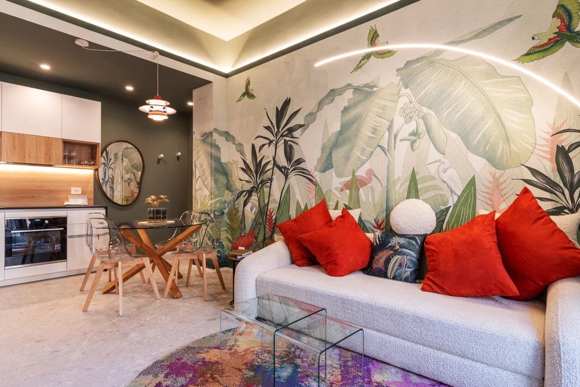 Vista angolata dell open space con cucina, tavolo in vetro, divano, carta da parati tropicale e illuminazione LED a soffitto