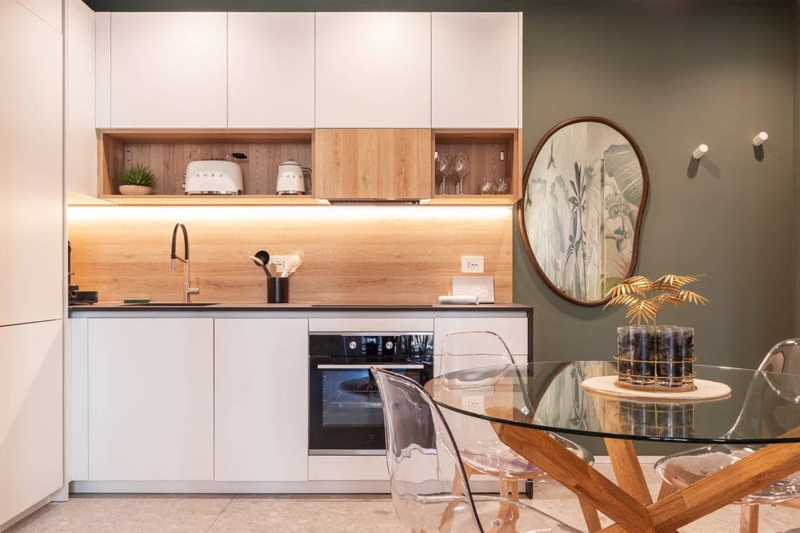 Angolo cucina bianco con paraschizzi in legno, elettrodomestici SMEG, forno incassato e specchio rotondo su parete verde