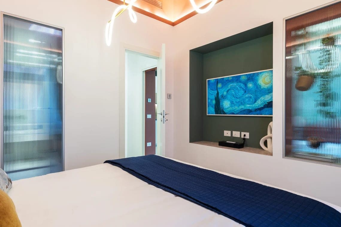Parete opposta della camera con schermo TV su nicchia verde, pannelli in vetro cannettato e luce neon scultorea