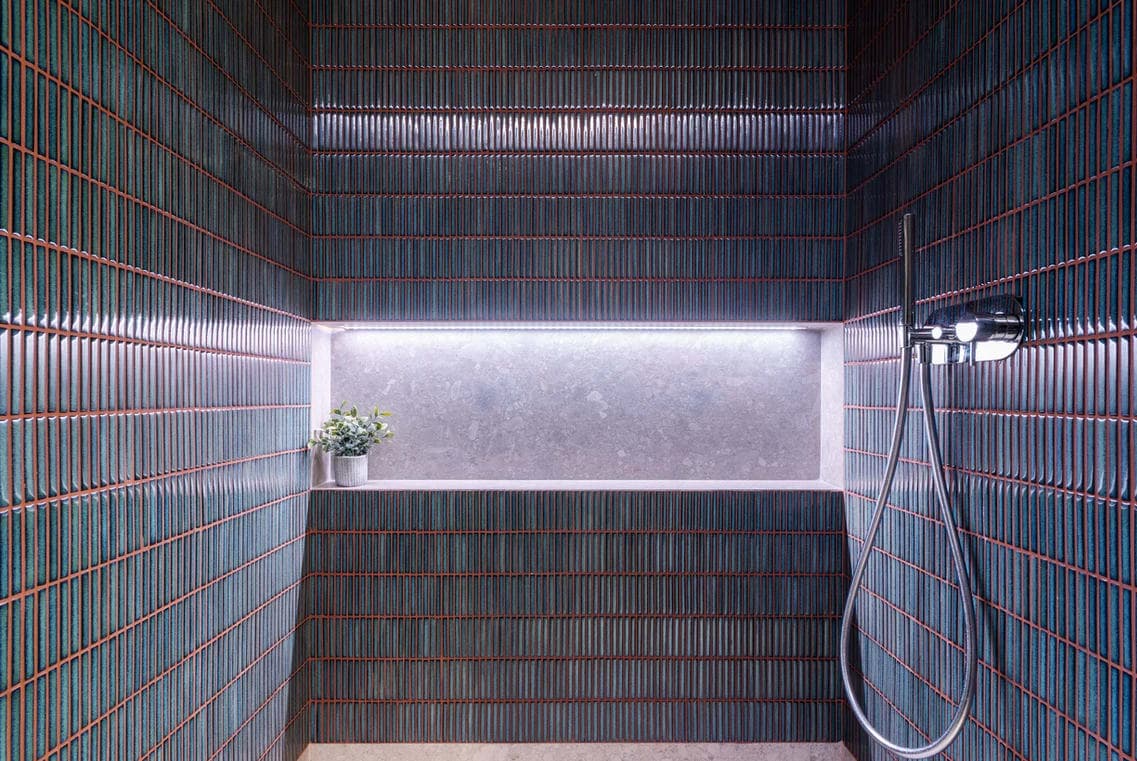Interno doccia con rivestimento in mosaico verde scuro, nicchia retroilluminata con pianta e soffione a mano