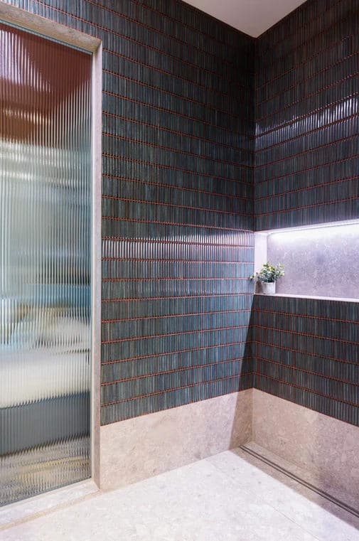 Ingresso doccia con porta in vetro cannettato, mosaico verde scuro e nicchia illuminata a parete