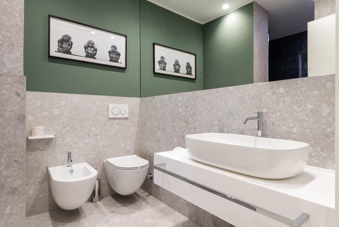 Bagno con pareti verde salvia, sanitari sospesi, lavabo a catino bianco e quadro decorativo a specchio
