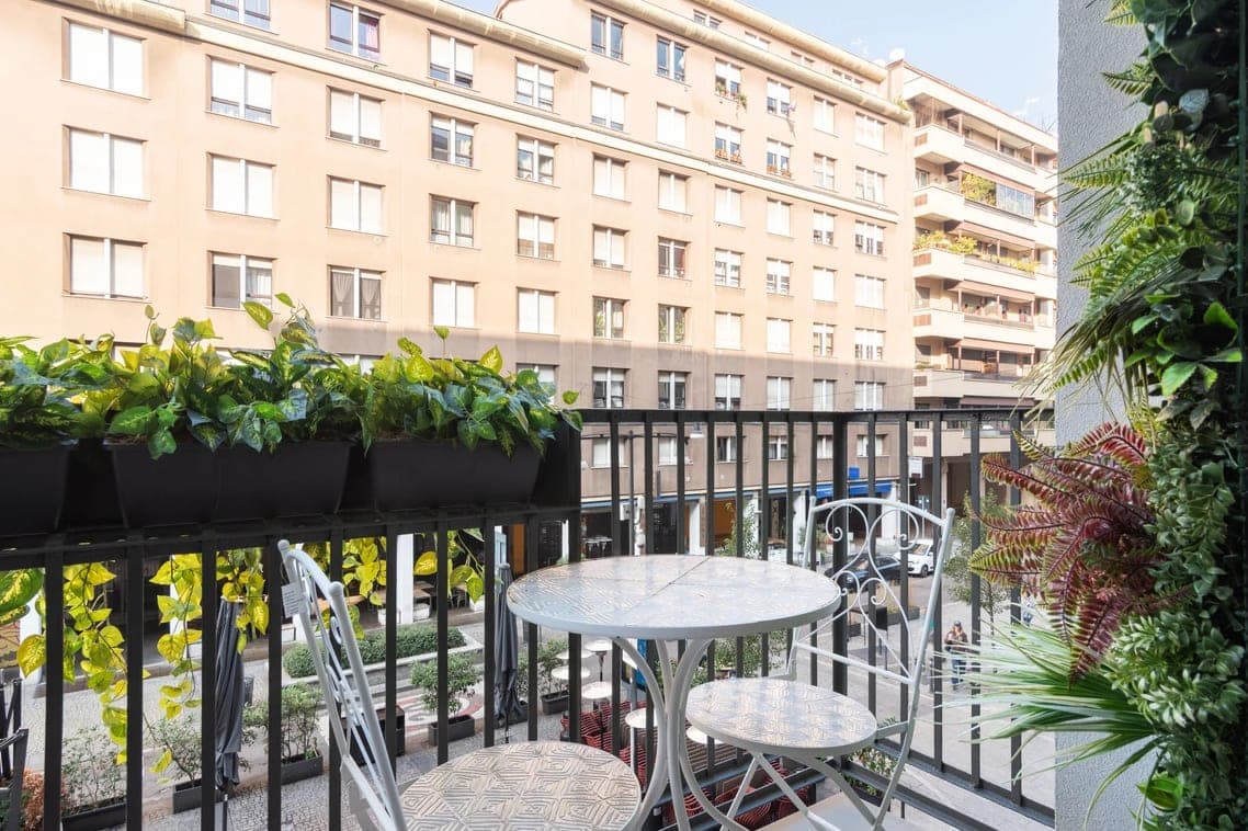 Balcone con vista su Corso Garibaldi, tavolino bistrot bianco, fioriere nere con rampicanti e parete verde verticale