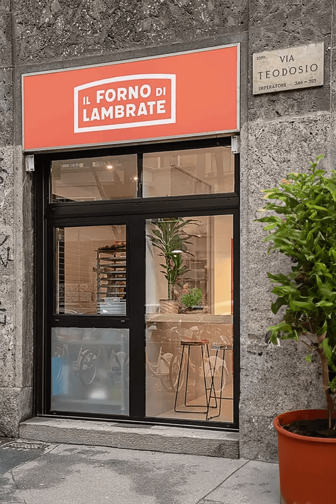 Фасад на Via Teodosio с красной вывеской Il Forno di Lambrate, стеклянный вход и традиционный миланский фасад