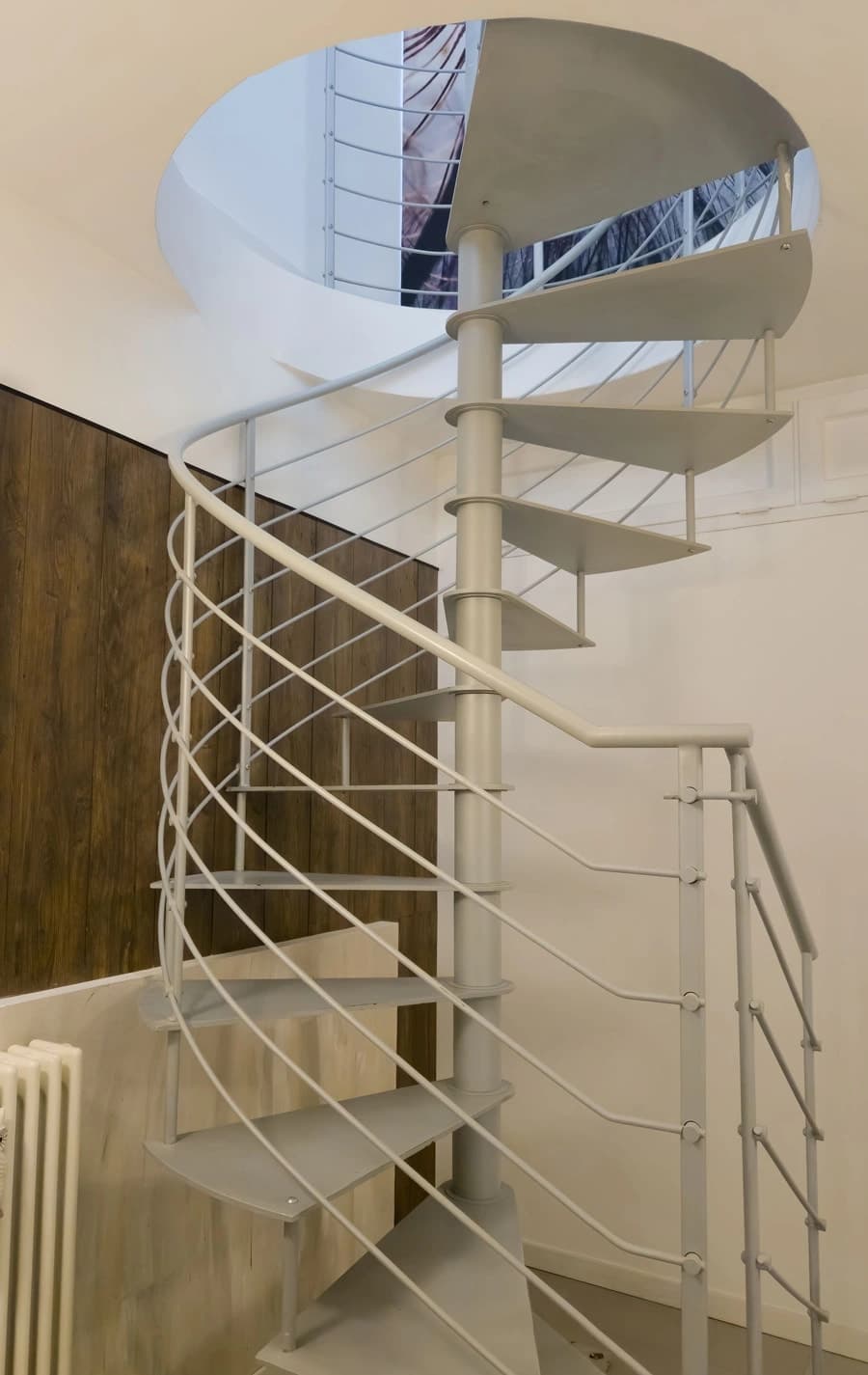 Escalier en colimaçon blanc avec rampe métallique et ouverture circulaire au plafond