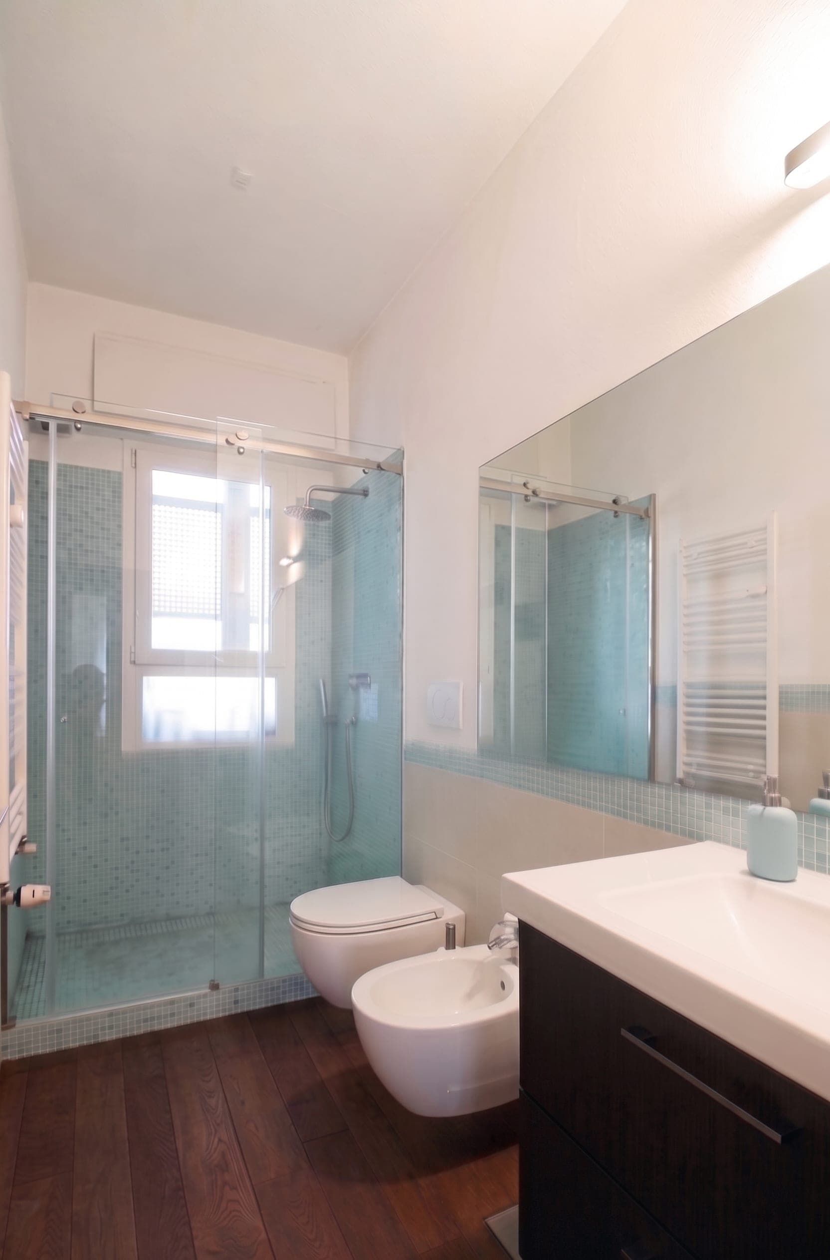 Bagno con doccia in vetro, mosaico azzurro, pavimento scuro e mobile lavabo