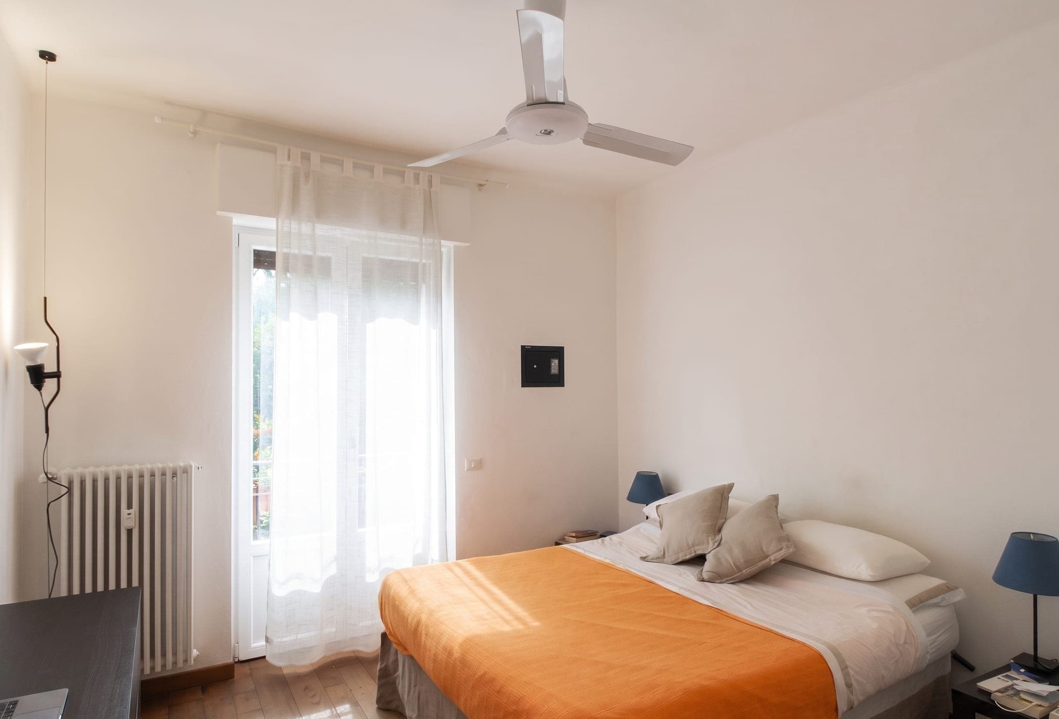 Camera da letto con copriletto arancione, ventilatore a soffitto e luce dalla portafinestra