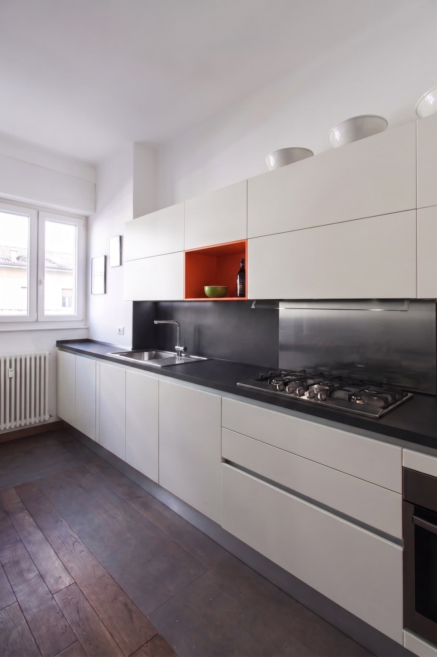 Vista completa cucina lineare con forno, nicchia arancione e tappeto colorato