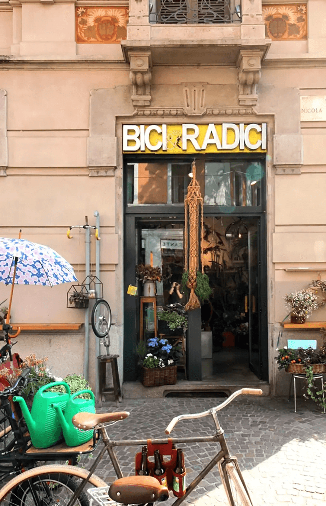 Exterior facade with Bici e Radici sign, parked bicycle and potted plants