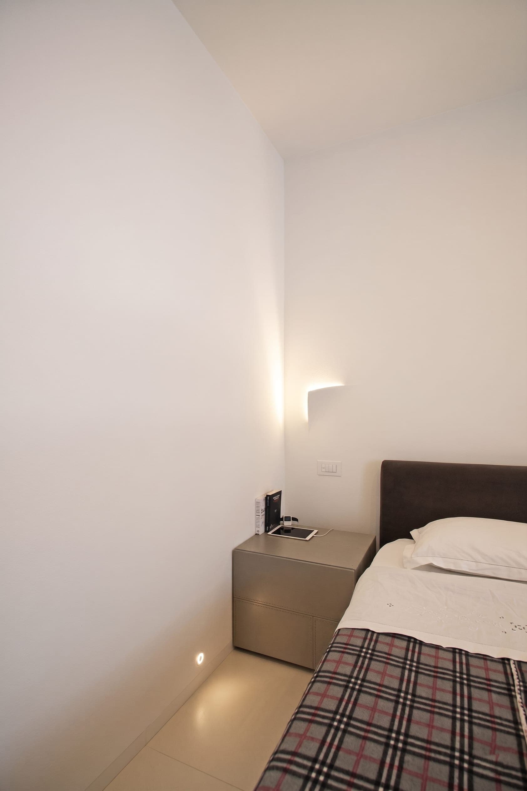 Angolo camera da letto con testiera imbottita scura e applique a parete