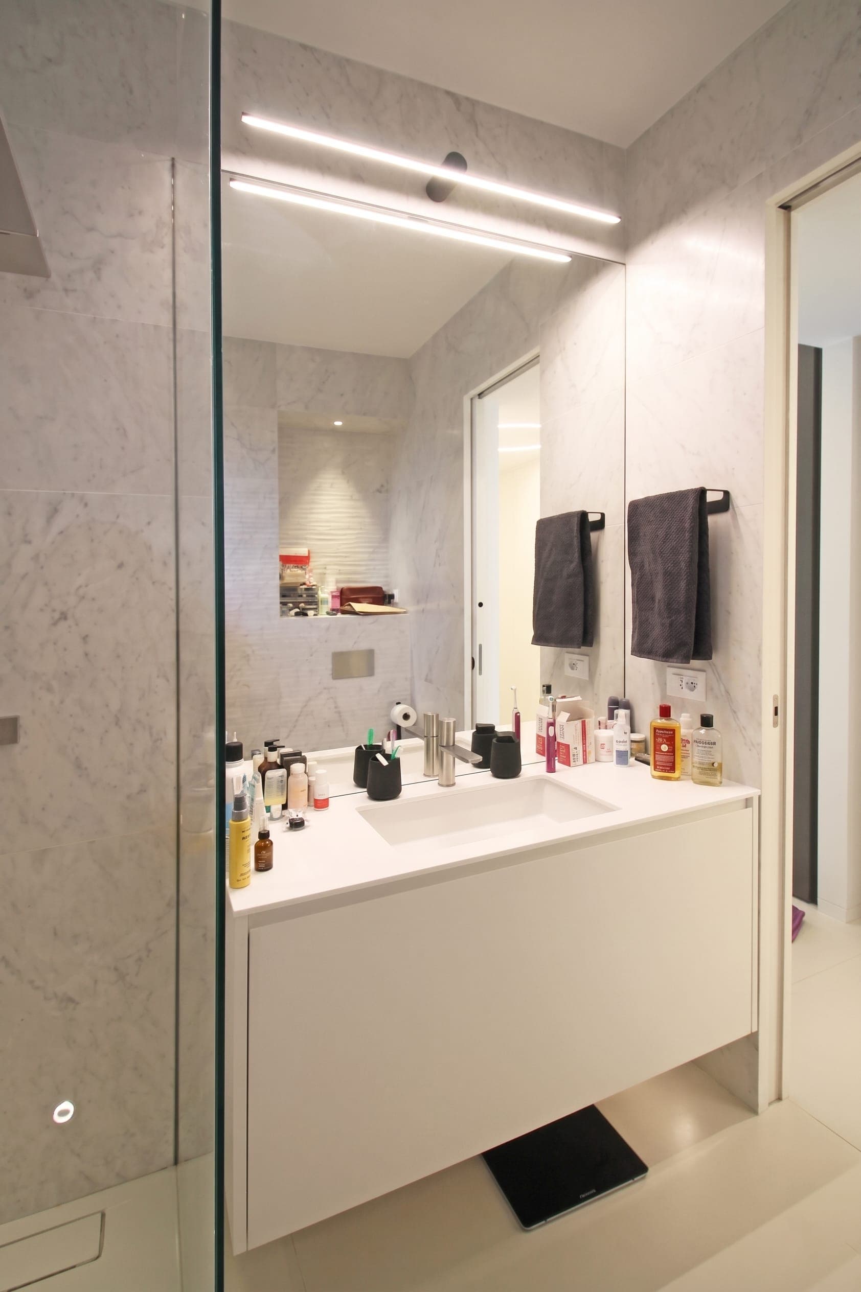 Bagno con doccia in vetro, mobile lavabo con accessori e portasalviette