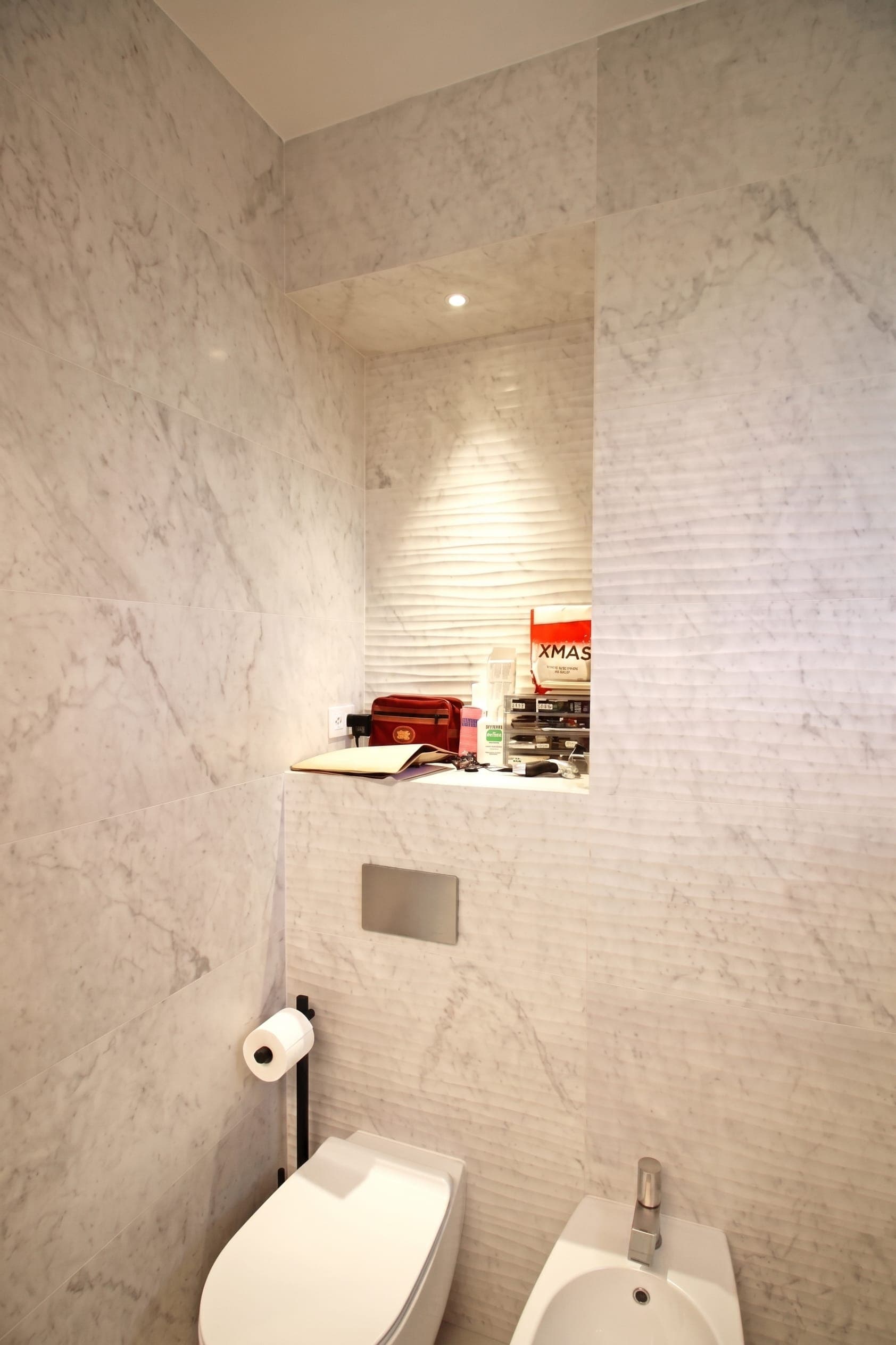 Dettaglio bagno con nicchia incassata illuminata e placca di scarico