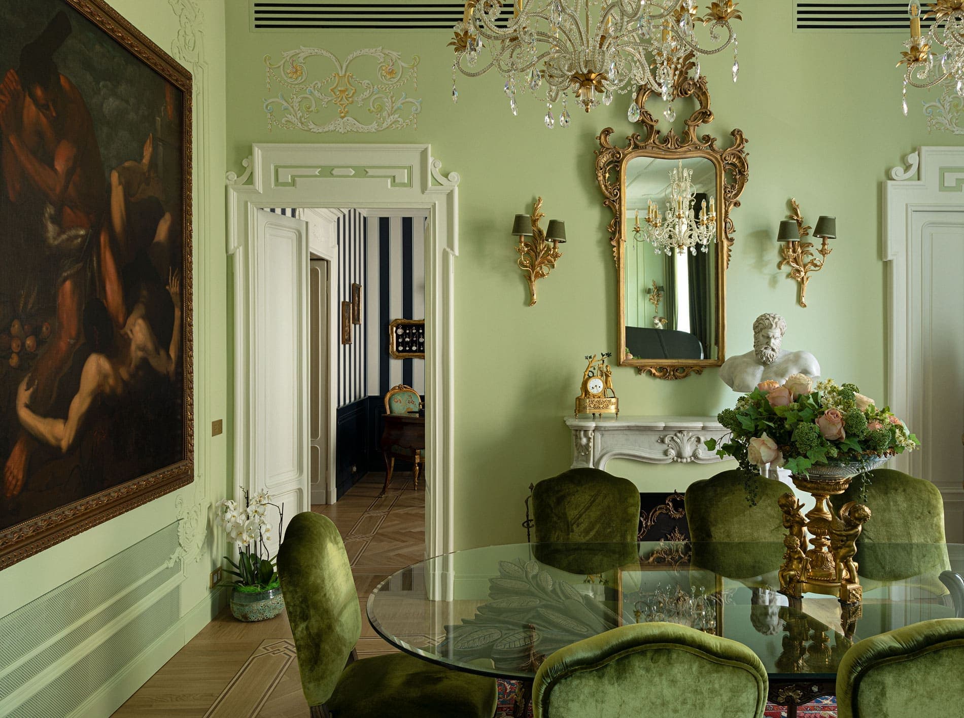 Dining room with sage green walls, golden chandelier, baroque mirror and velvet chairs
