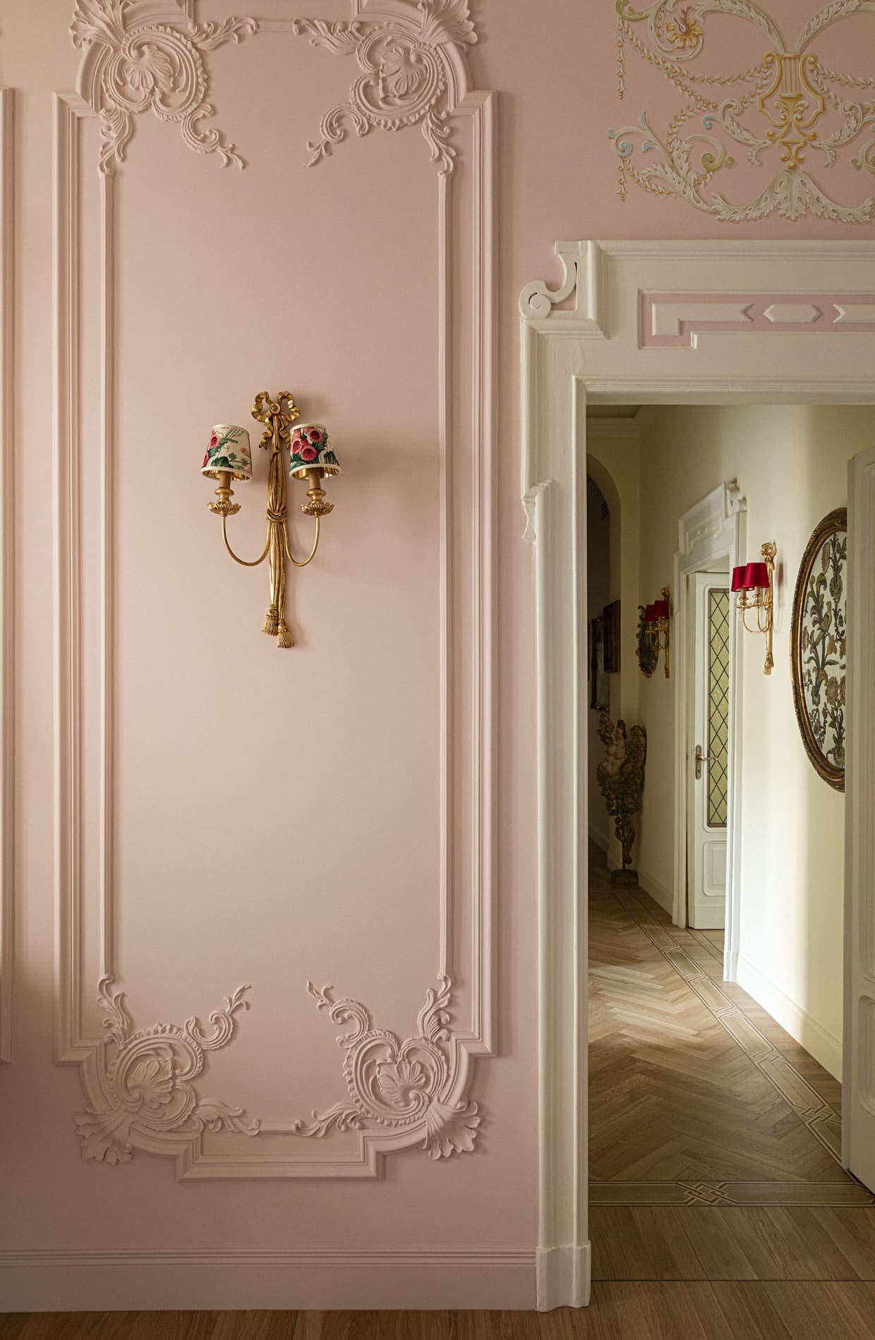 Pink wall with rococo stucco, golden porcelain wall sconce and historic hallway