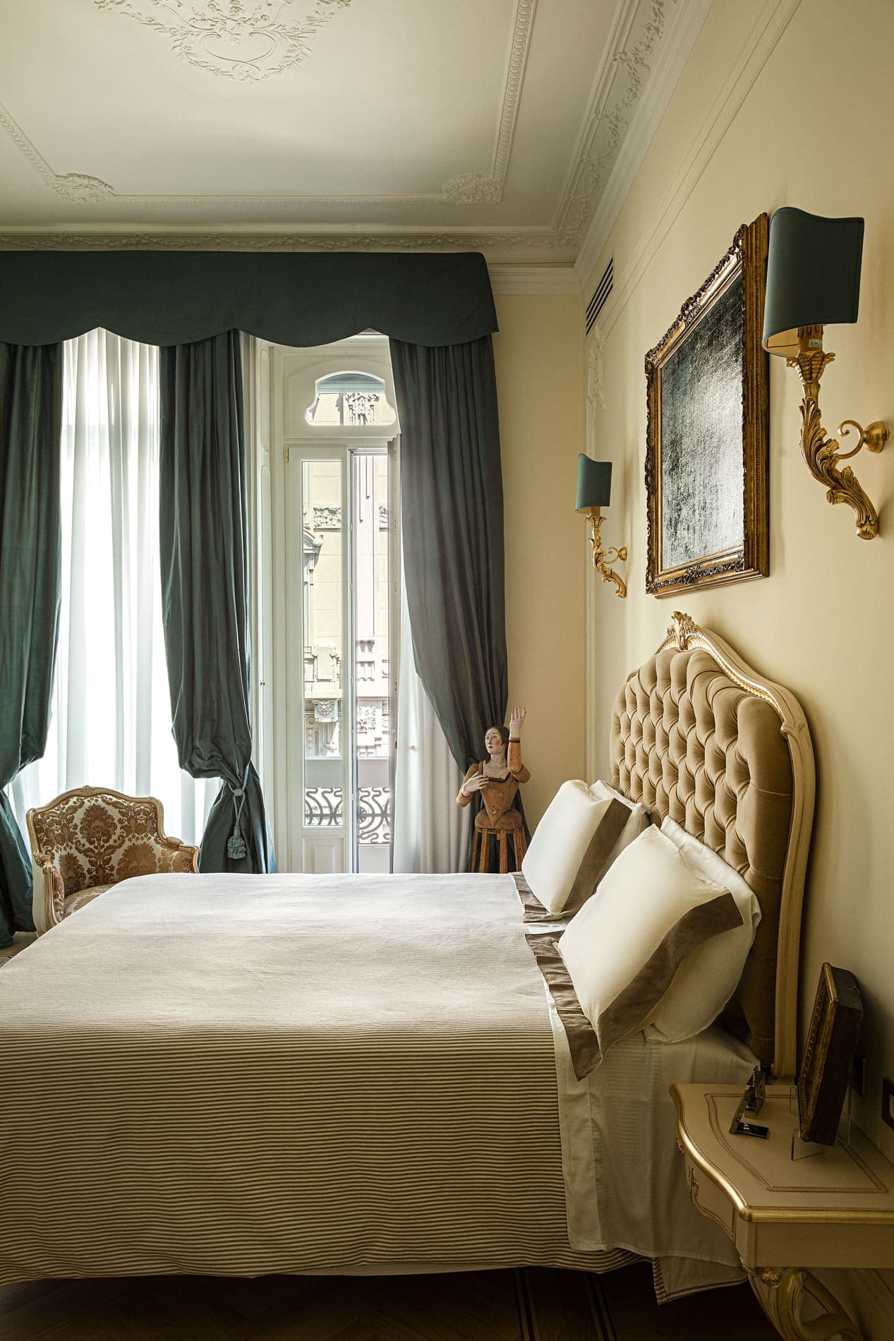 Bedroom with golden tufted headboard, green curtains and period armchair