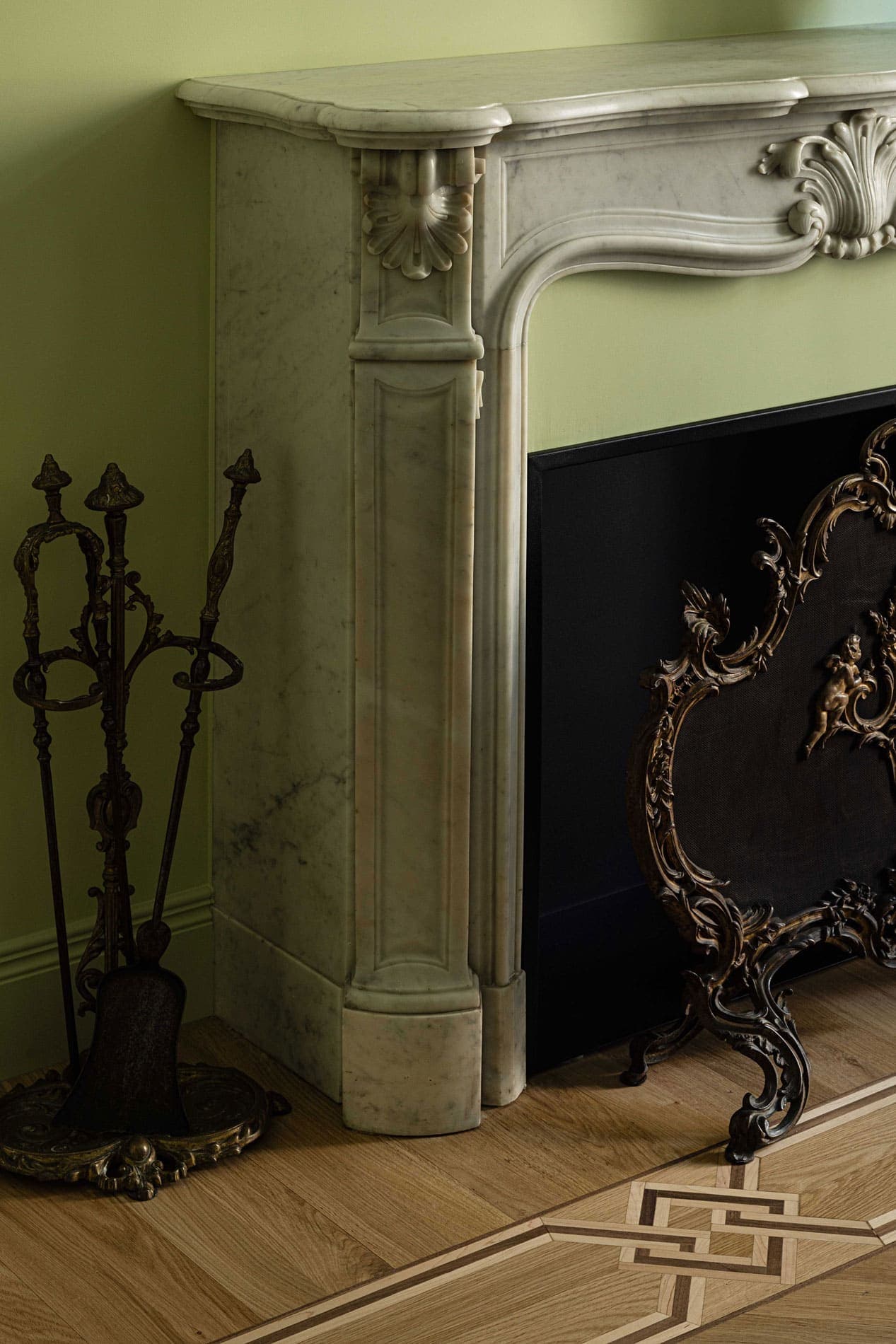 Fireplace detail with carved surround, bronze fire screen and inlaid parquet