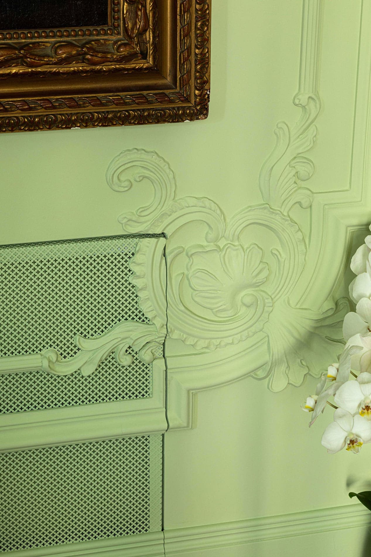 Detail of restored rococo stucco with radiator cover grille on sage green wall