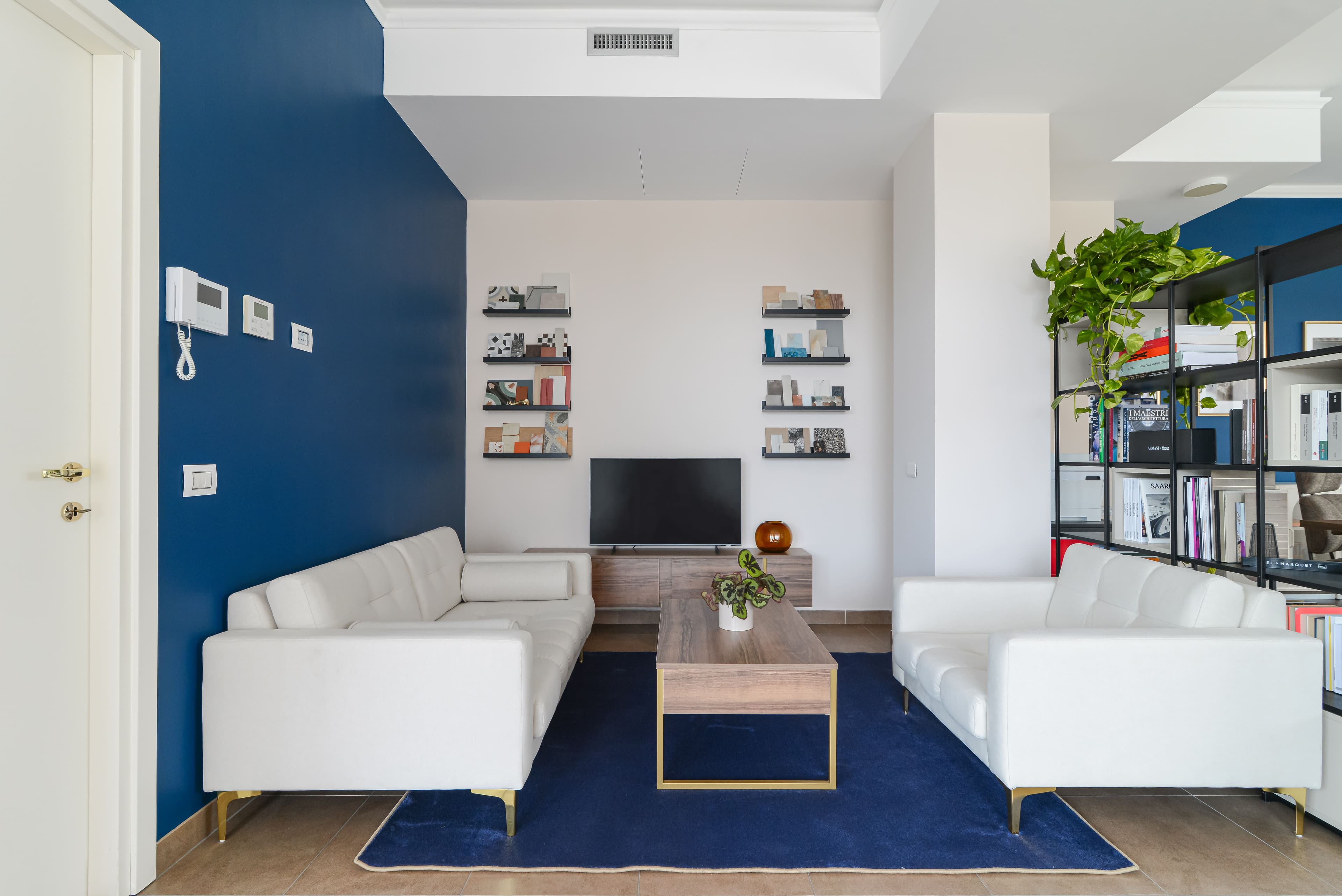 Area lounge con divani bianchi, parete blu e mensole con campionature di materiali