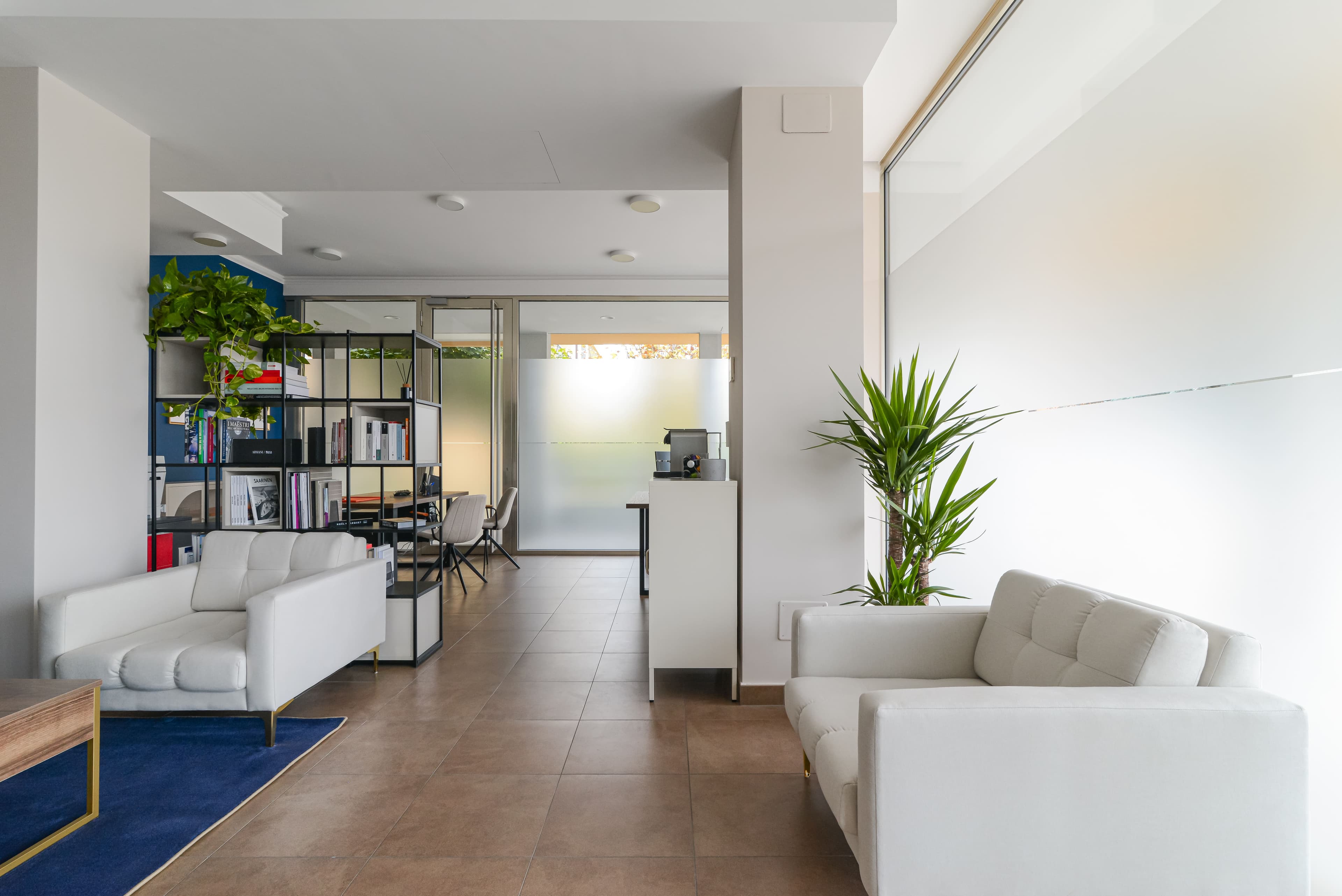Vista laterale dello showroom con divani bianchi, libreria e vetrata smerigliata