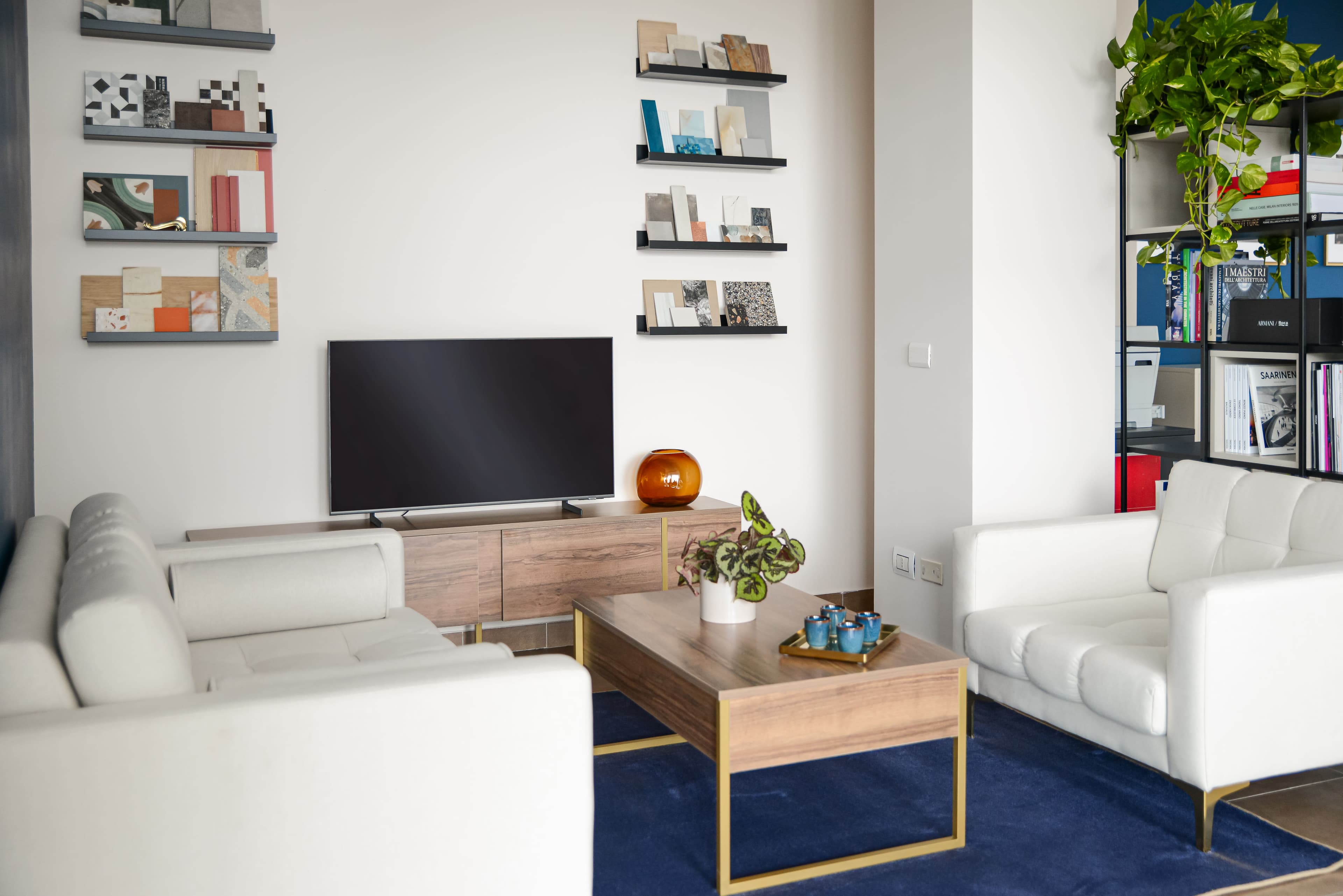 Area lounge frontale con divani bianchi, tavolino e campionature a parete