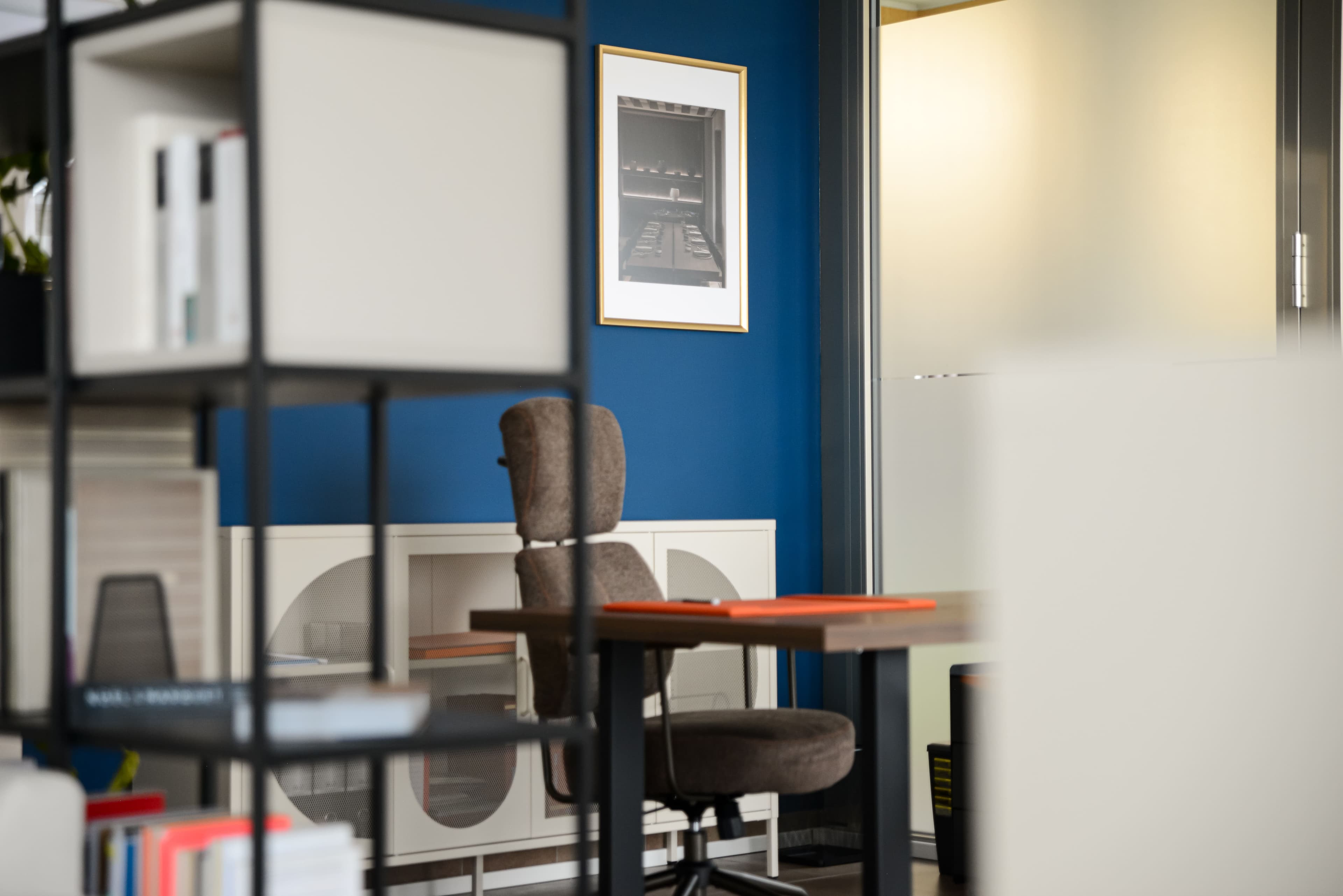 Ufficio visto attraverso la libreria, scrivania con sedia ergonomica e parete blu