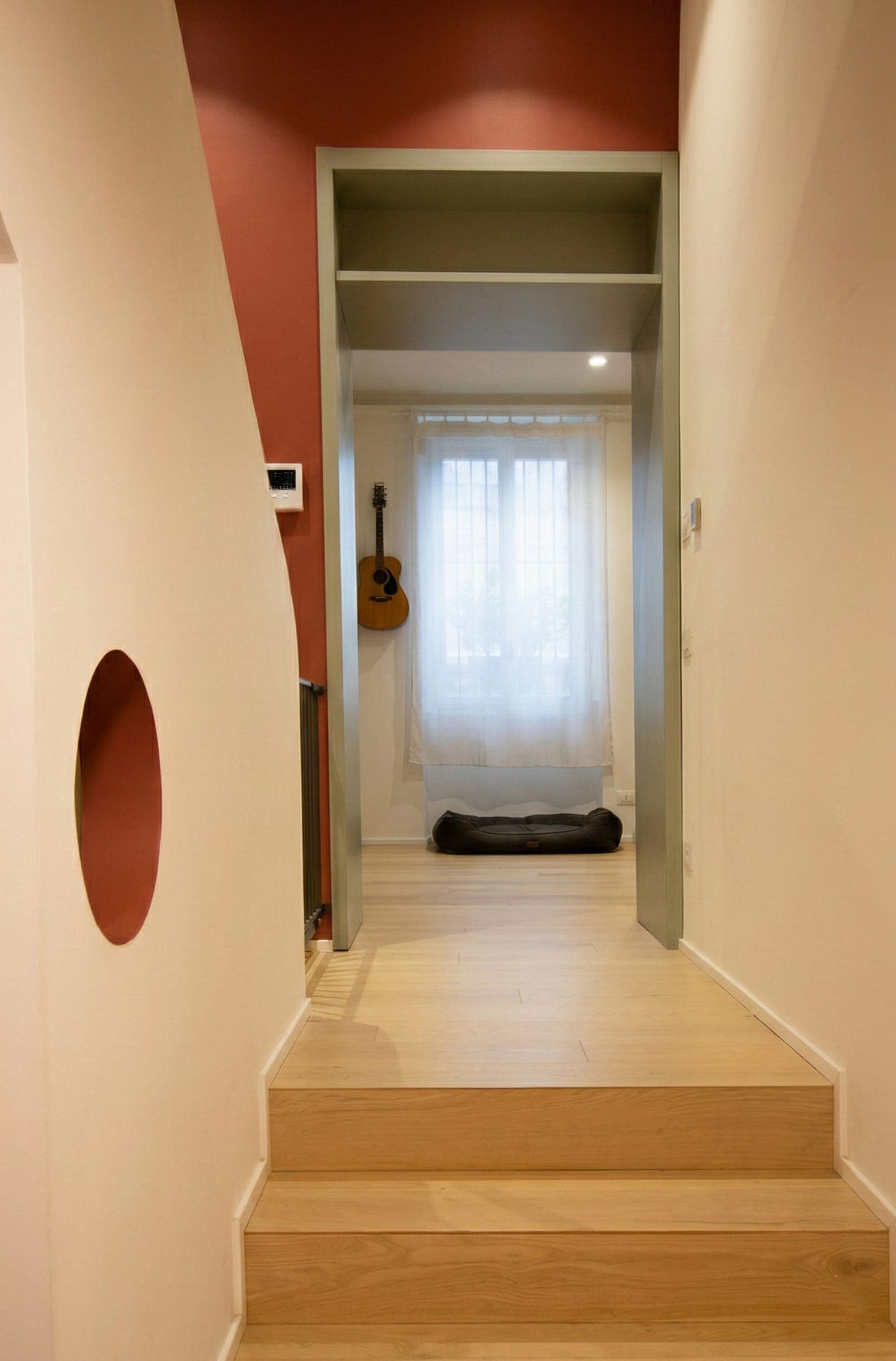 Corridoio con elemento decorativo rotondo rosso a parete e porta vetrata