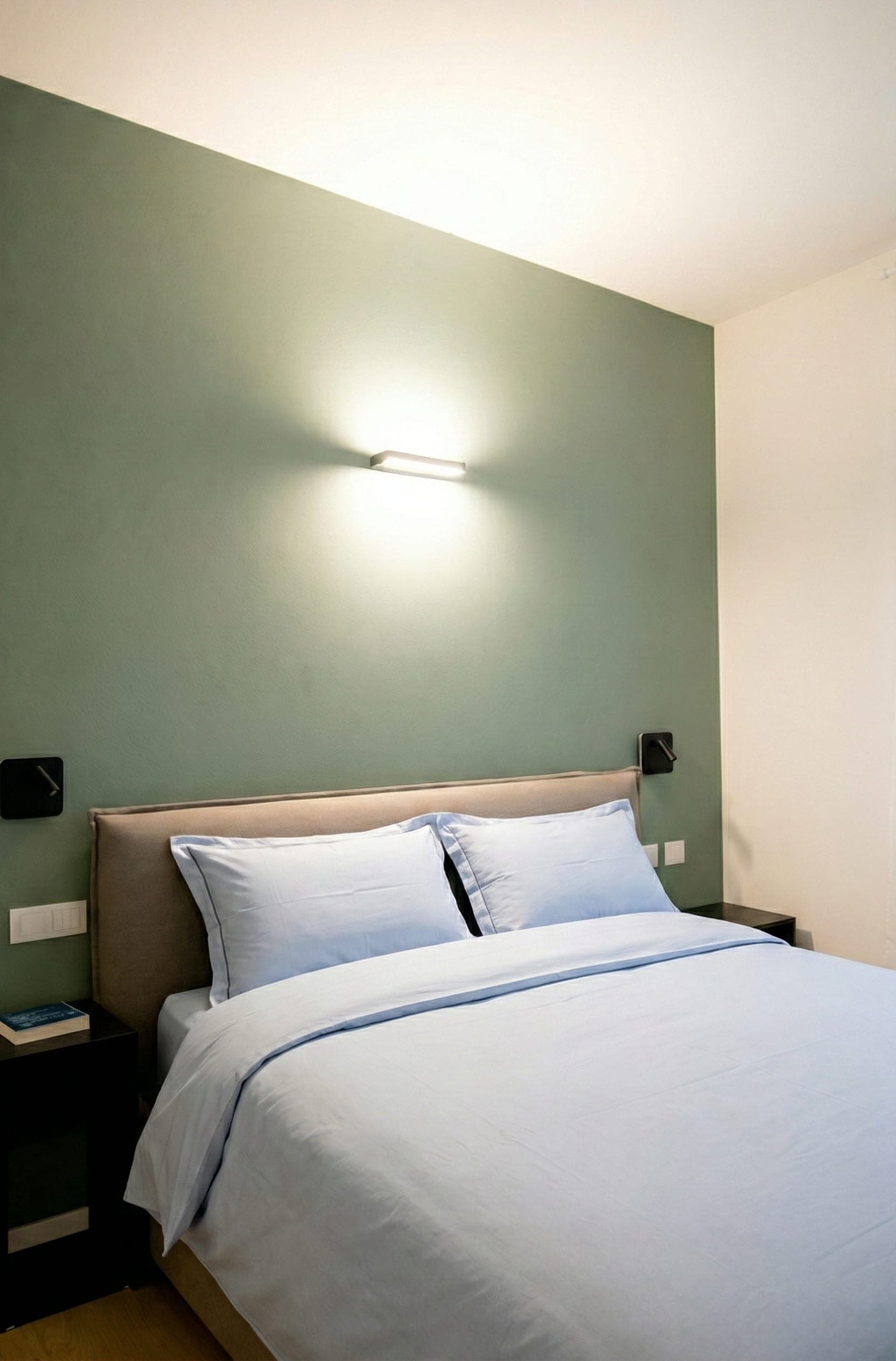 Camera da letto con parete verde salvia, applique e biancheria azzurra