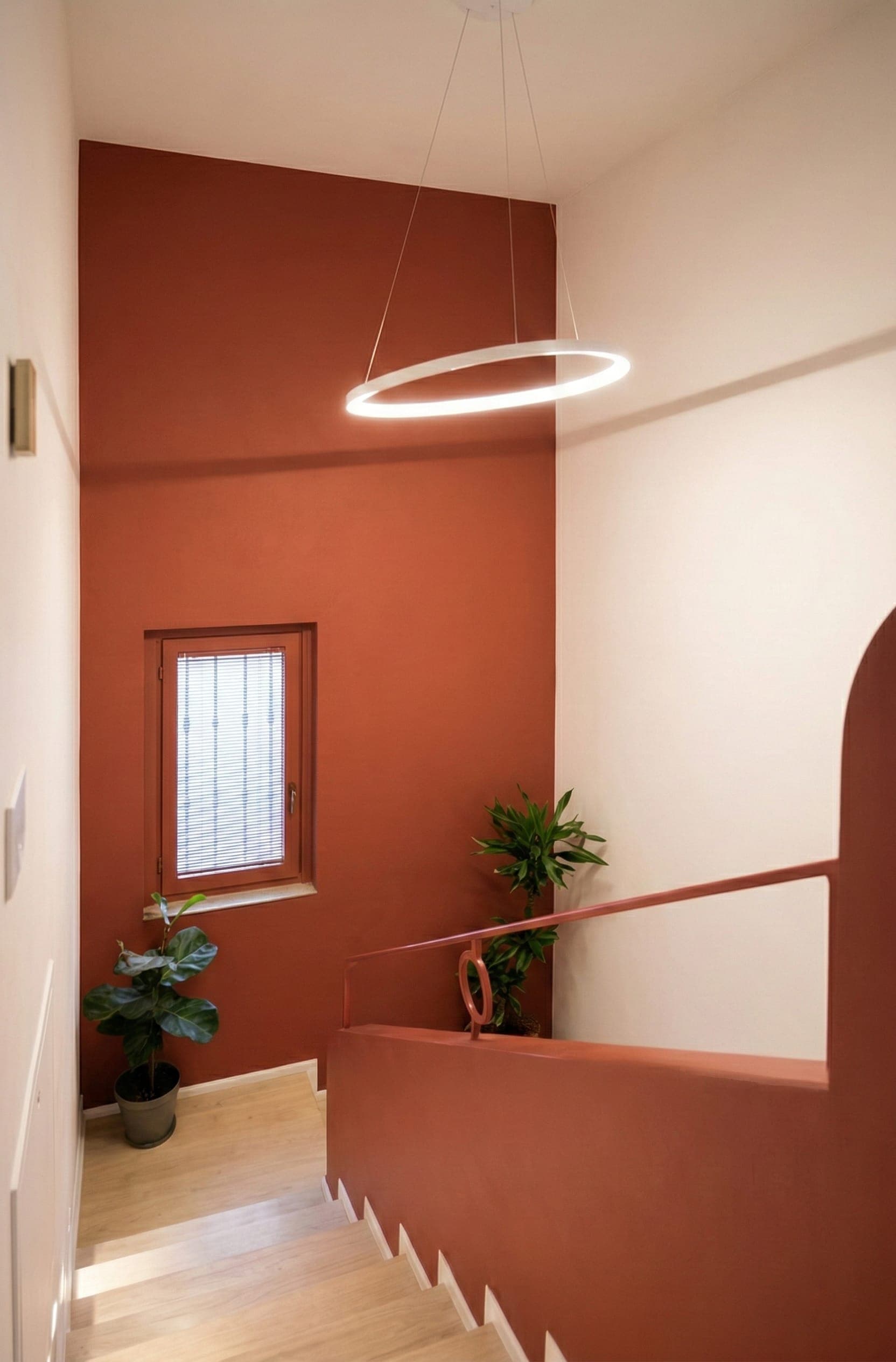 Vano scala con parete color terracotta, finestra e piante verdi