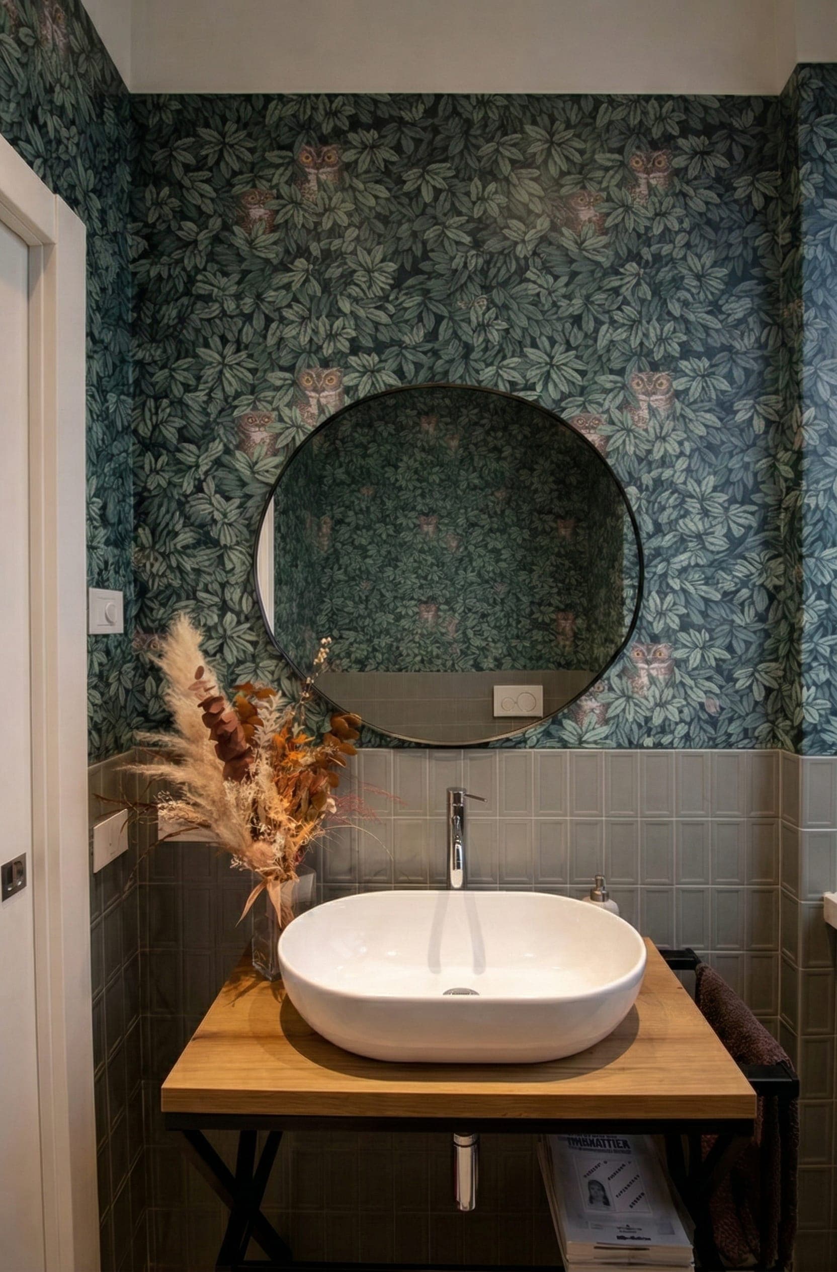Bagno con grande specchio rotondo, carta da parati botanica e lavabo a catino