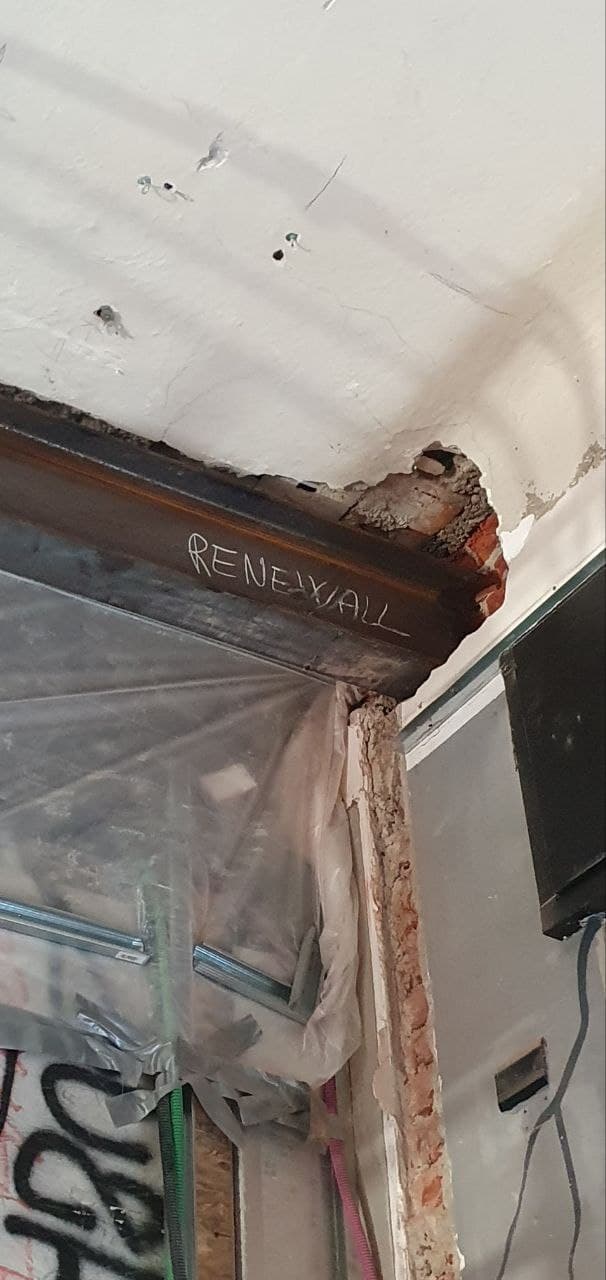 Fase di cantiere: dettaglio trave con scritta RENEWALL a gesso, muratura a vista e impianti elettrici