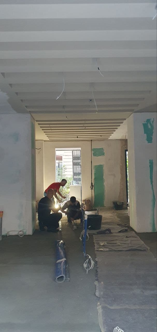 Fase iniziale del cantiere con operai al lavoro sul pavimento, soffitto a travi e campioni colore a parete