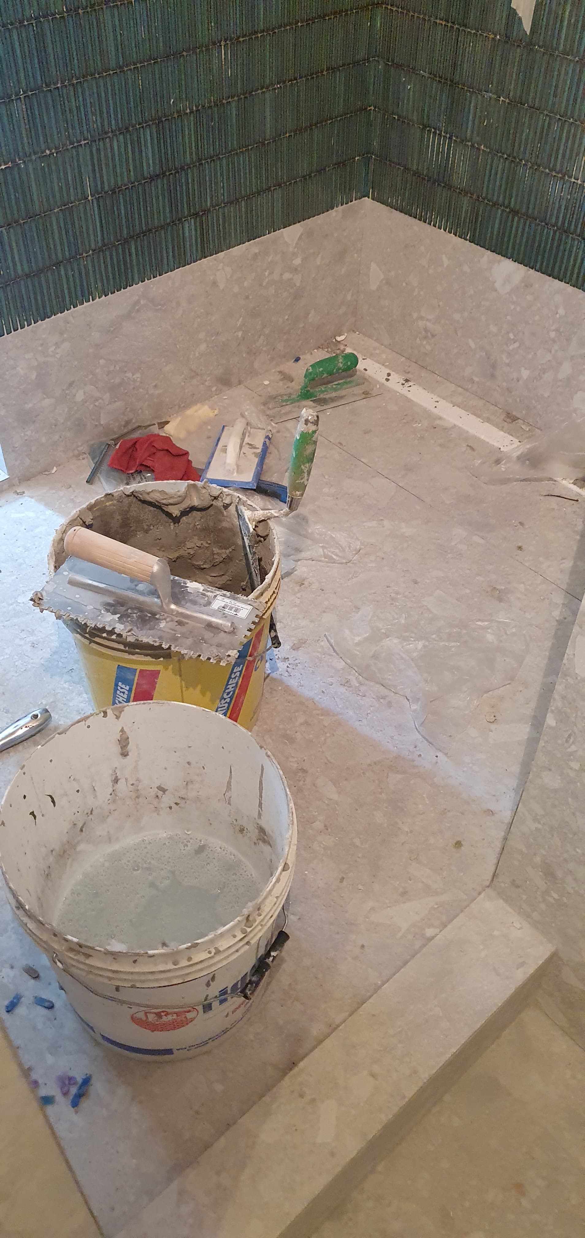 Fase di cantiere: dettaglio pavimento doccia in lavorazione con secchi, attrezzi e mosaico verde scuro a parete